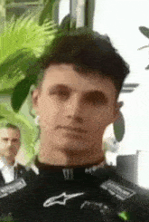a close up of a man 's face with a plant in the background and a man standing behind him .