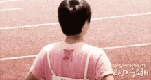 a man in a pink shirt is walking on a track and looking at the camera .