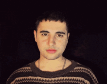 a man wearing a sweater and a chain around his neck looks at the camera