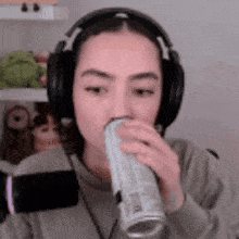 a woman wearing headphones is drinking from a can of soda .