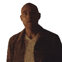 a bald man wearing a brown jacket and a white sweater looks at the camera