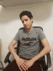 a young man wearing a hollister t-shirt sits in a chair