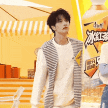 a man wearing a striped vest is standing in front of a large bottle of orange juice .