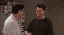 two men are standing next to each other in front of a refrigerator and shaking hands .