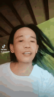 a man with long hair is wearing a white shirt and has a tiktok logo on the bottom right