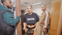a woman in a zeus t-shirt is standing in a doorway