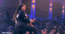 a woman in a number 16 jersey is dancing on a stage in front of a crowd