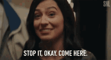 a woman is smiling and saying stop it okay come here .