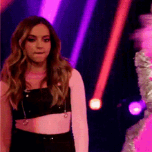 a woman in a crop top stands in front of a purple and pink light