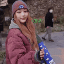 a girl wearing a beanie and a jacket is holding a skateboard and smiling .