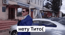 a man in a suit and sunglasses is standing next to a silver car .