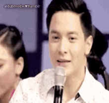 a man is talking into a microphone with a woman in the background .
