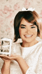 a woman in a white top is smiling and holding a can of volcanic ash
