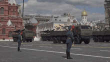 a man in a red hat stands in front of a row of military trucks
