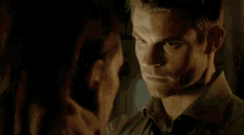a man is touching a woman 's face in a dark room with a lamp in the background .