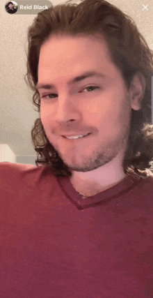 a man with long hair and a beard is wearing a red shirt with the name reid black on the bottom right