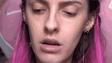 a woman with pink hair and earrings is making a funny face .