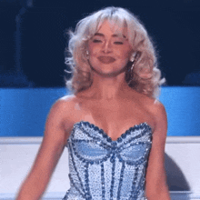 a woman in a blue dress with a bow on the front is smiling