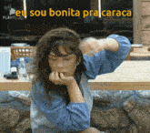 a woman sitting at a table with the words eu sou bonita pra caraca