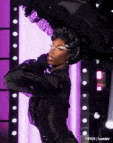 a woman in a black dress is dancing on a stage with purple lights behind her