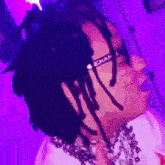 a man with dreadlocks and glasses is wearing a white shirt and a purple background .