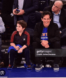 a man and a boy are sitting on the sidelines of a basketball game .