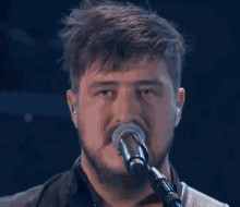 a man with a beard singing into a microphone with his eyes closed