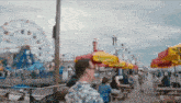 a man walking down a boardwalk with a ferris wheel in the back