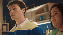 a man in a blue yellow and white striped shirt stands next to a woman with curly hair