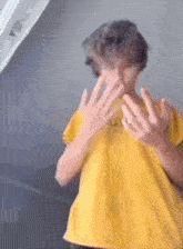 a young boy in a yellow shirt is making a funny face with his hands .