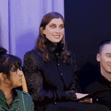 a woman in a black shirt smiles while sitting next to a man in a black shirt