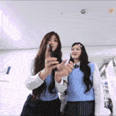 two girls are standing next to each other and one of them is holding a cell phone