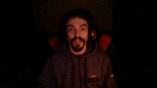 a man with a beard wearing a nike sweatshirt is smiling in the dark