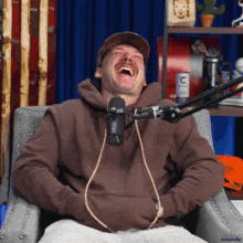 a man wearing a brown hoodie is laughing in front of a microphone with the letter c on it