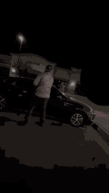 a man is opening the door of a black car in a parking lot