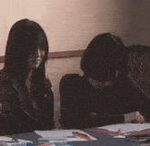 two women are sitting at a table looking at papers .
