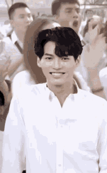 a man in a white shirt is standing in front of a crowd of people and smiling .