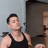 a man in a black tank top is eating a pizza in a room .