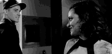 a man and a woman are looking at each other in a black and white photo . the woman has a tattoo on her arm .