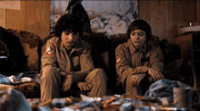 two boys in ghostbusters costumes sit on a couch in a messy room