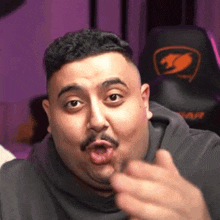 a fat man with a mustache is pointing at the camera .