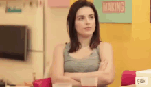 a woman is sitting at a table with her arms crossed in front of a sign that says making