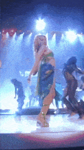 a woman in a green dress is dancing on a stage with other dancers