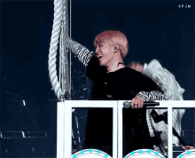 a man with pink hair and wings is holding a microphone and laughing while standing on a balcony .