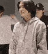 a young man wearing a gray hoodie is standing in a room with other people .