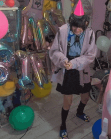 a girl wearing a pink party hat stands in a room filled with balloons