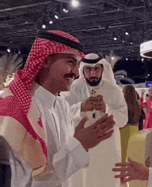 a man in a keffiyeh smiles while another man holds his phone