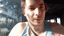 a man wearing a blue tank top and a necklace looks at the camera