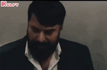 a man with a beard is wearing a suit and white shirt and looking down .