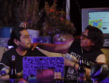 a man wearing a black shirt with the word lui on it is talking to another man